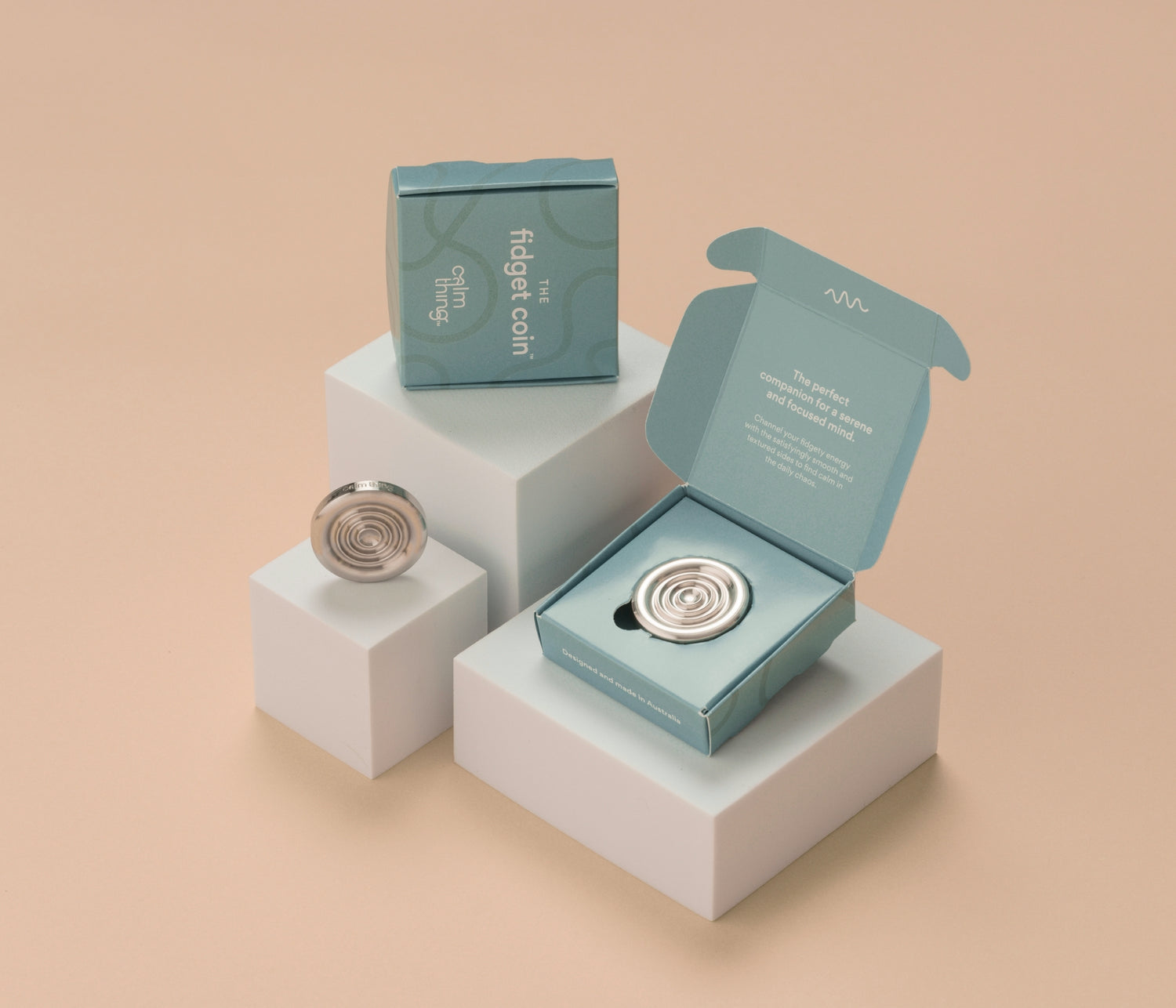 Fidget coins displayed on white blocks, one on its own and two in blue boxes, with a beige background. 